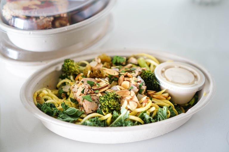 A fresh takeout salad in molded fiber bowl with broccoli, almonds, and dressing, perfect for a healthy meal. - Dogfish Packaging
