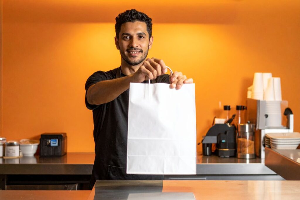 Human holding a takeout bag in a cafe.