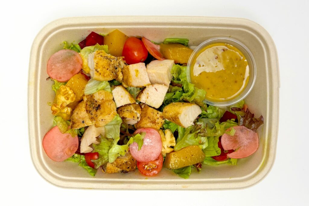 Overhead view of molded fiber rectangular bowl filled with a salad and cut chicken.