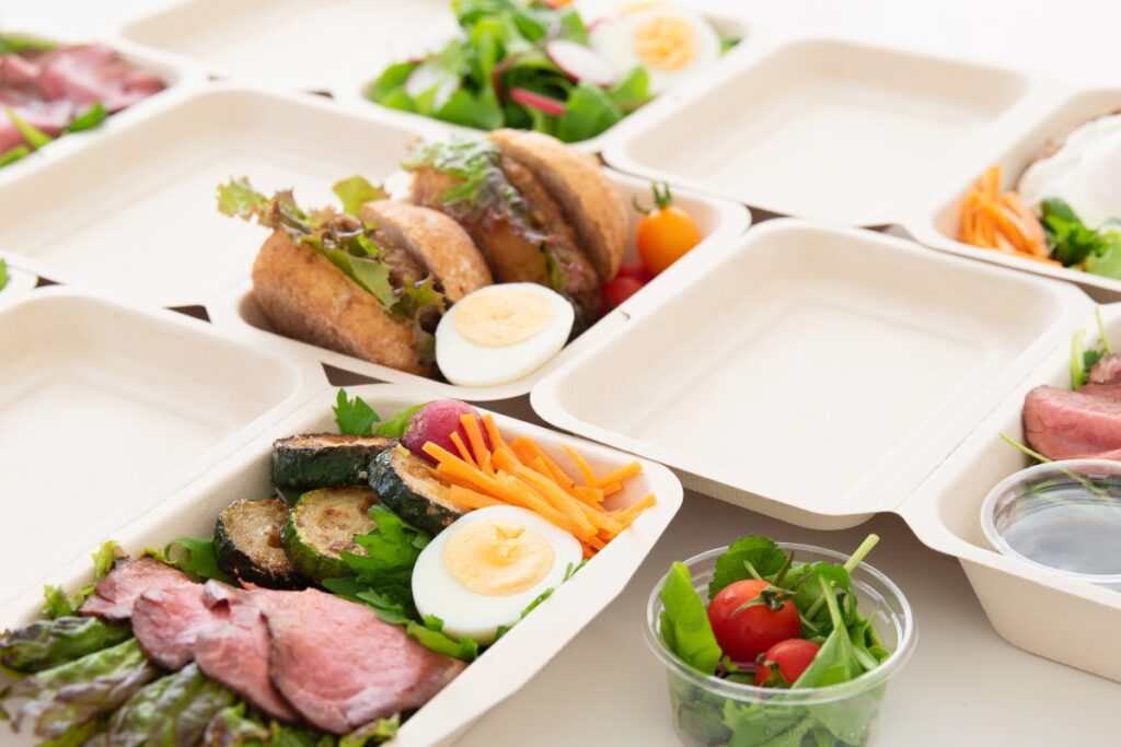 Several molded fiber takeout containers with vegetables, burgers, and more.