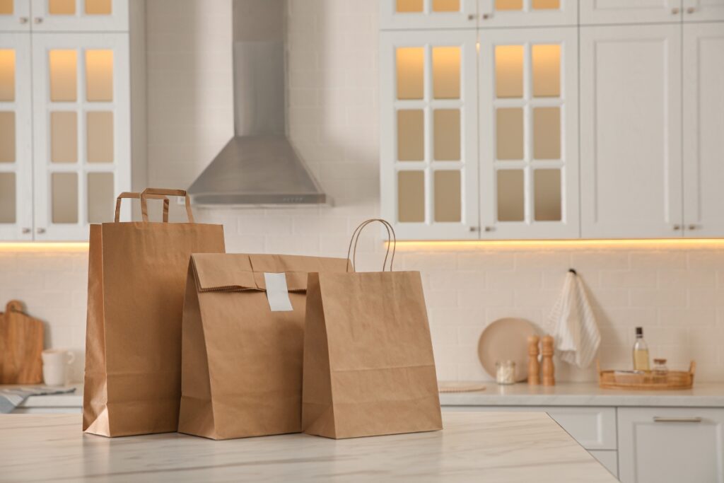 Three takeout brown paper bags on a kitchen counter.